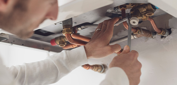 A technician working on plumbing connections under a boiler installation.