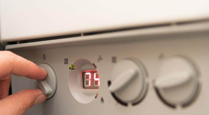 Hand adjusting the temperature control on a heating unit displaying 74 degrees.