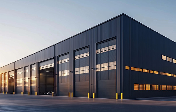 Modern industrial building with large windows and overhead doors, with a sunset backdrop.