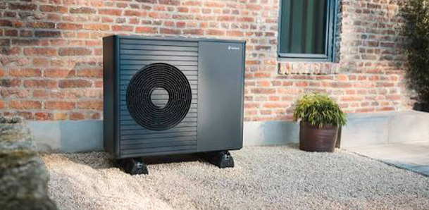 Heat pump installation outside a brick building with gravel and greenery.